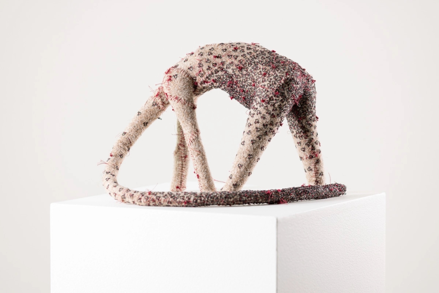 Felt sculpture of creature covered in black pins and red stitches