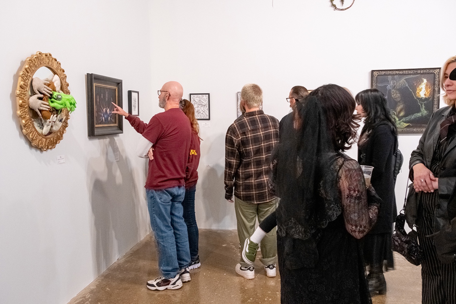 Visitors in an art gallery point at works on the wall