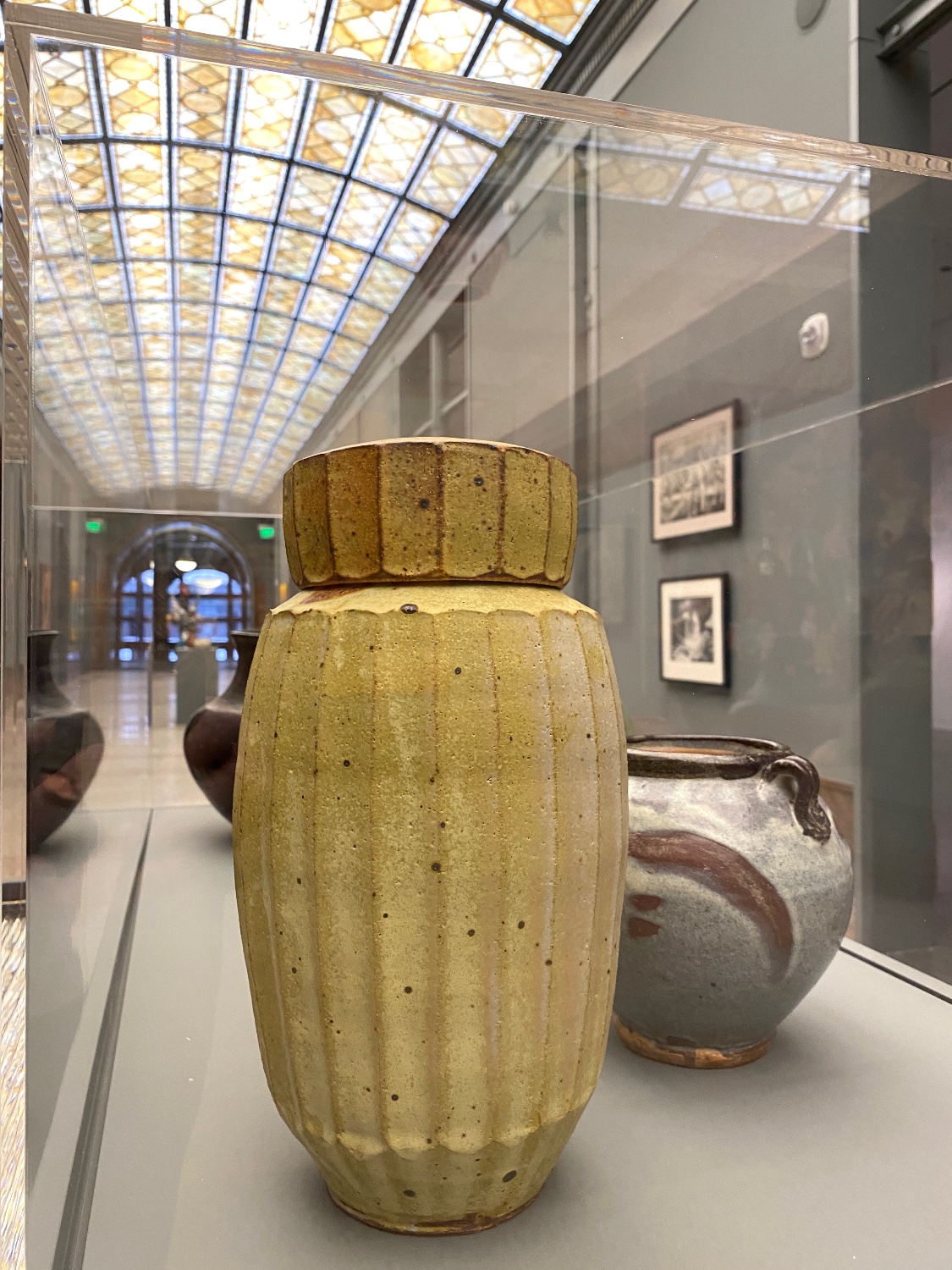 Display case of ceramic vessels under a yellow stained glass ceiling