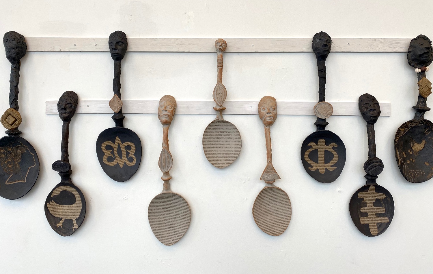 Black and white ceramic spoons hang on the wall with faces for handles and patterned words on their spoon bowls