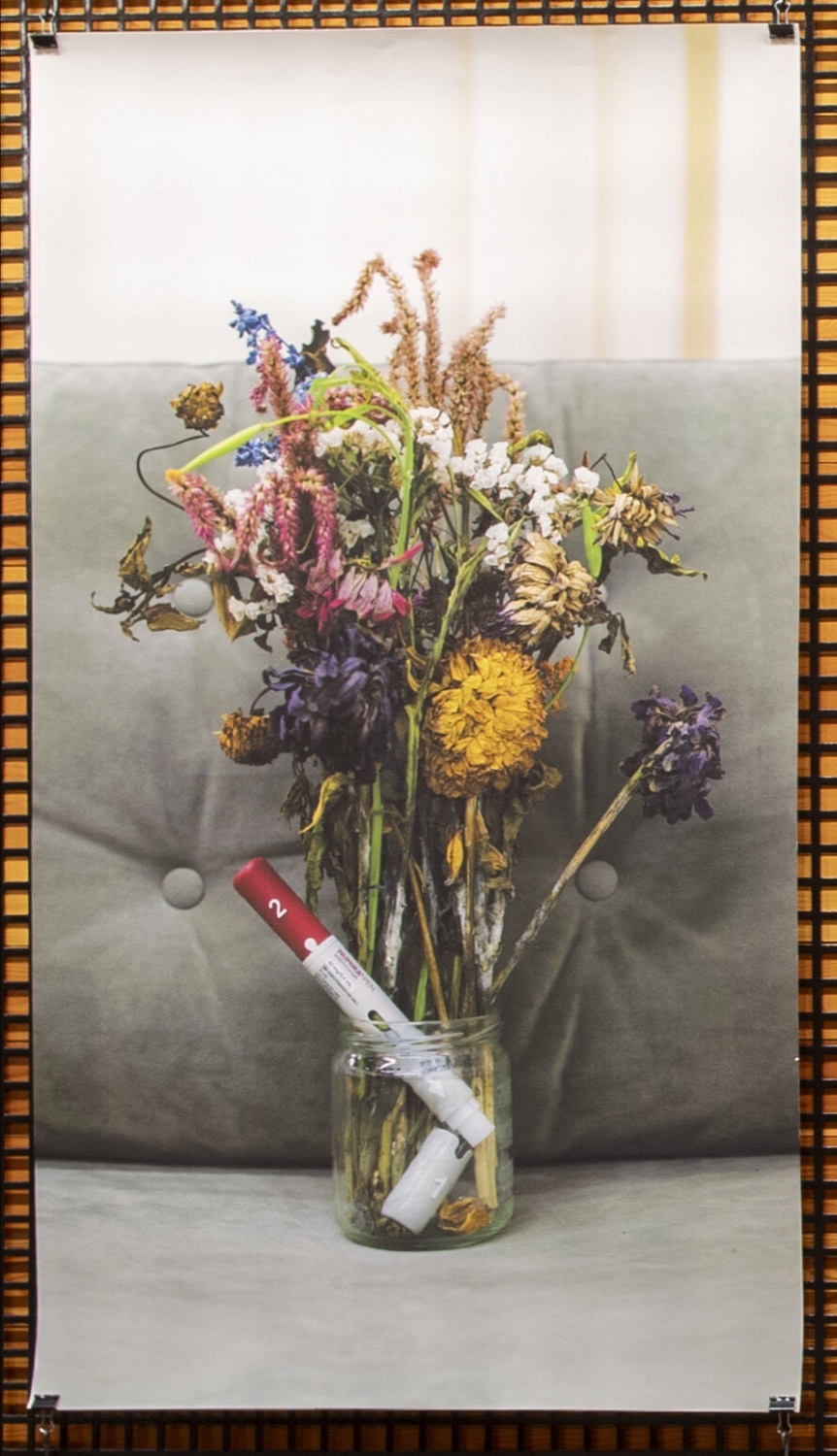 A display of dying flowers in a glass jar with a white and red Humira applicator
