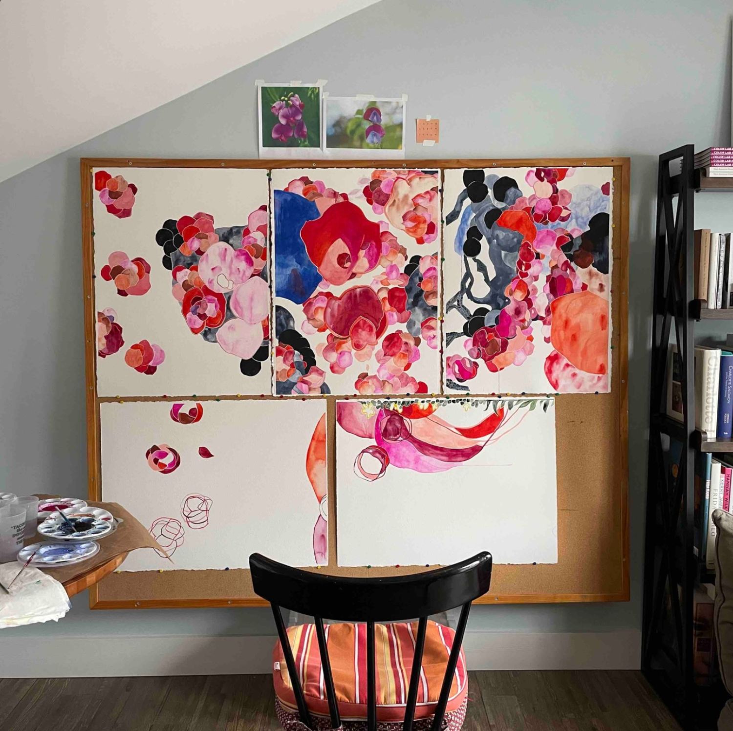 A home art studio with abstract flower paintings on a drawing board next to a chair and bookshelf