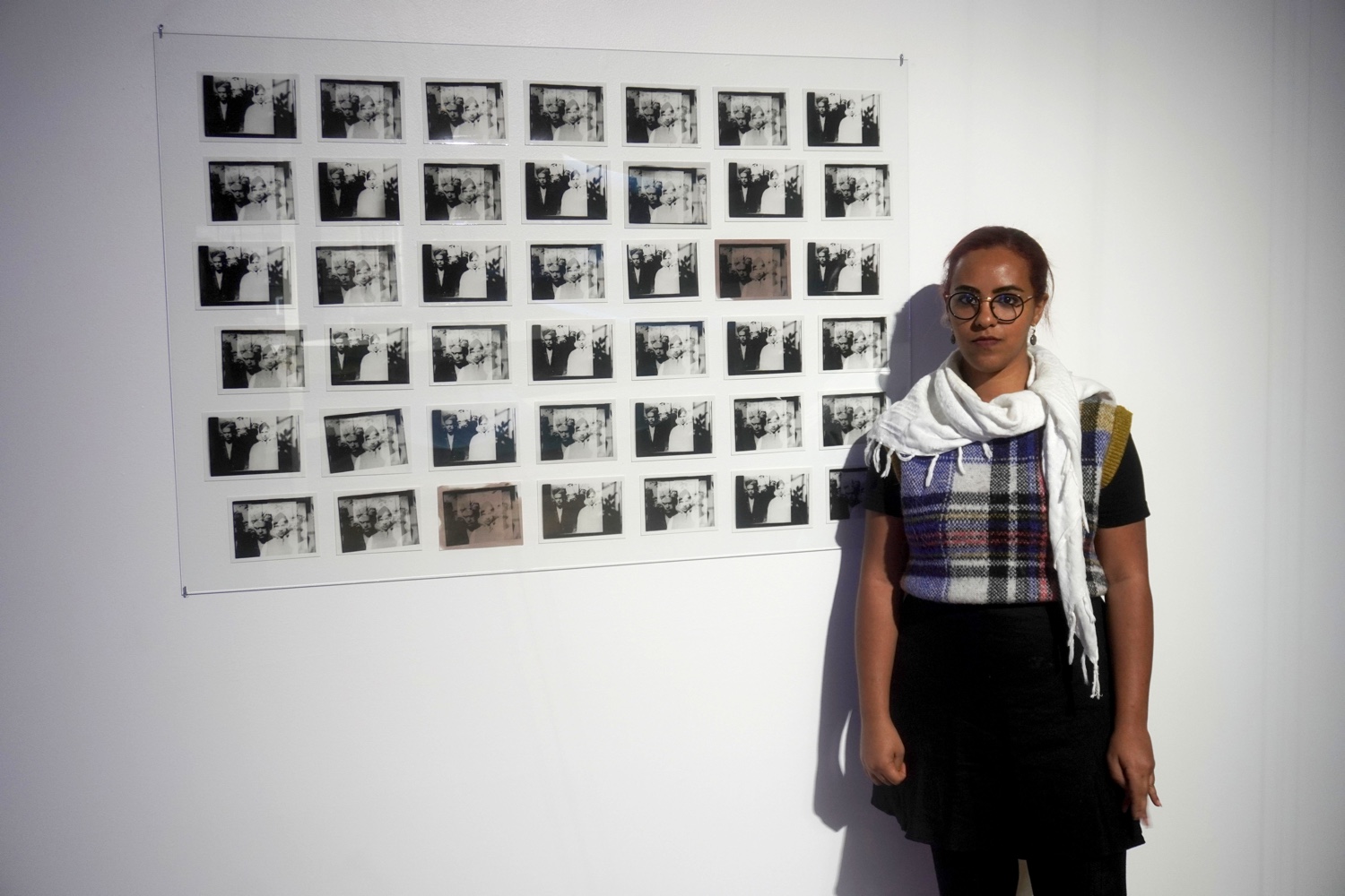 A woman stands next to a grid of black and white photos