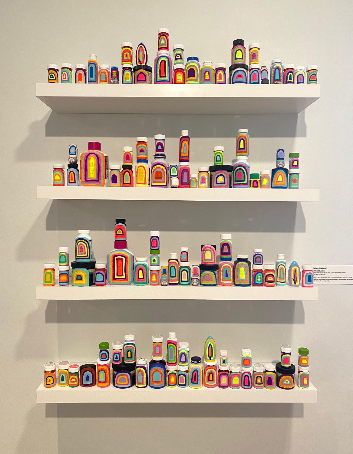 Four shelves filled with small bottles painted in multicolored patterns