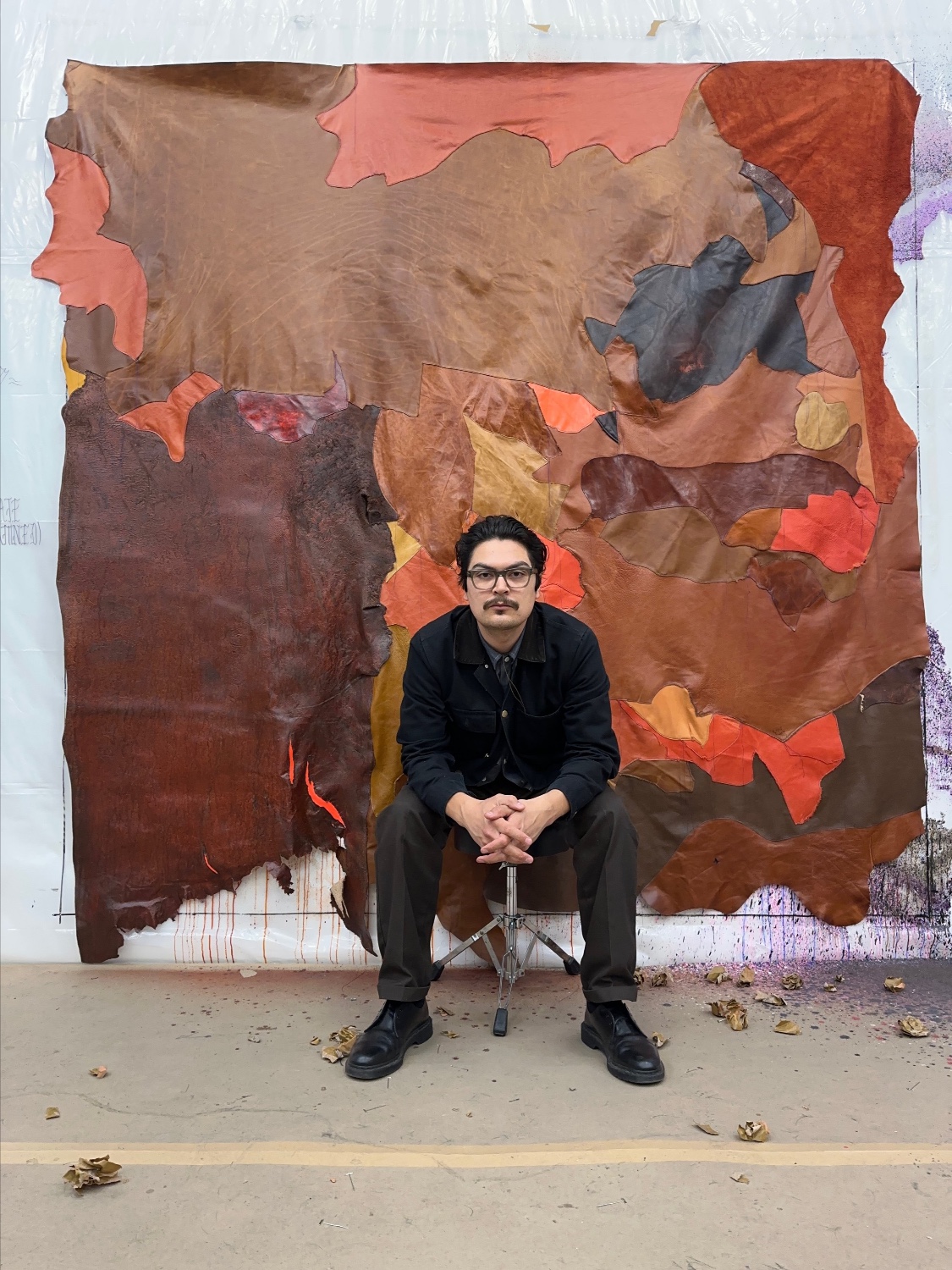 Man sits in front of tapestry made of brown fabric and leather