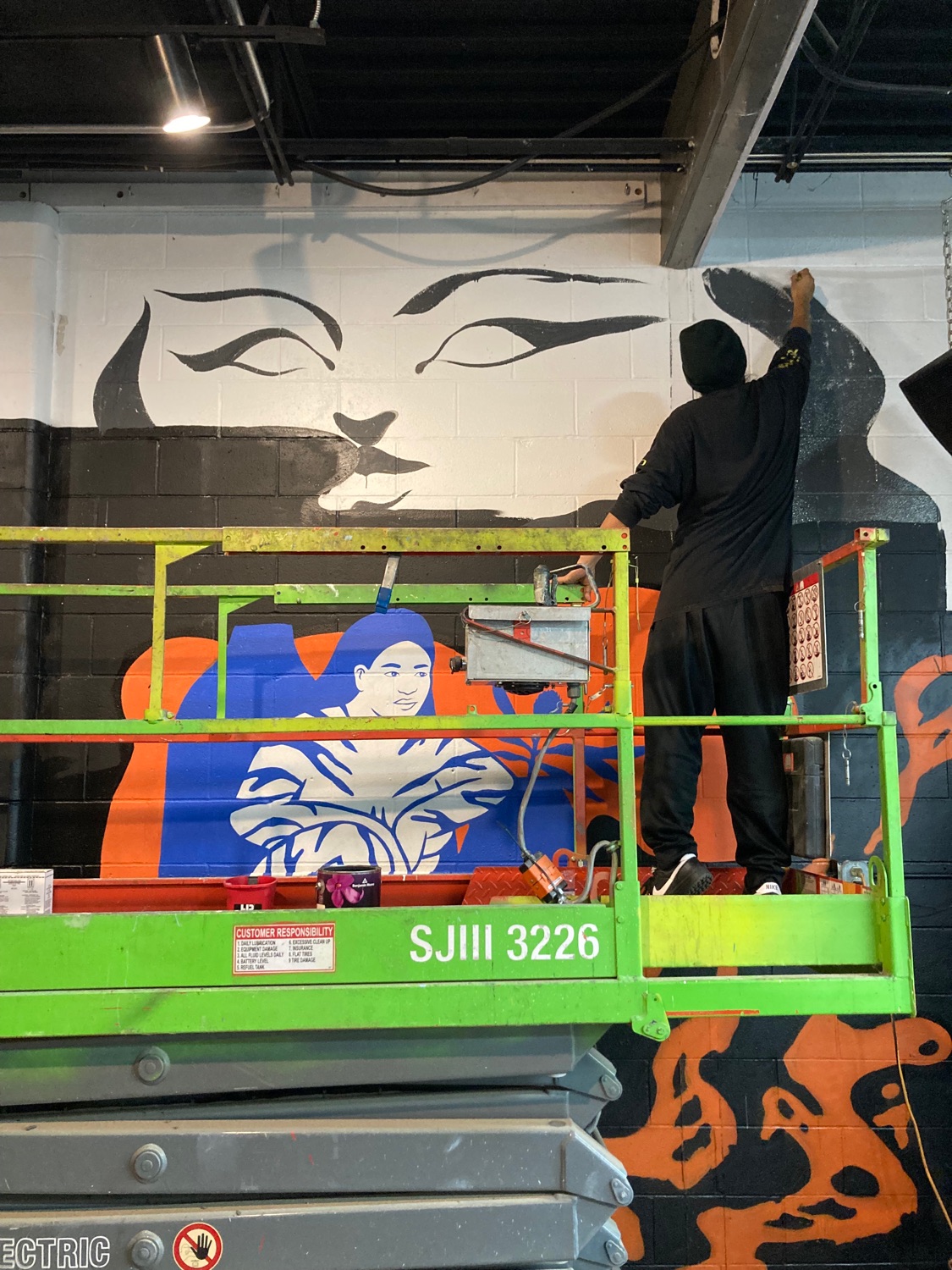 Person on a scissor lift painting a mural on a brick wall