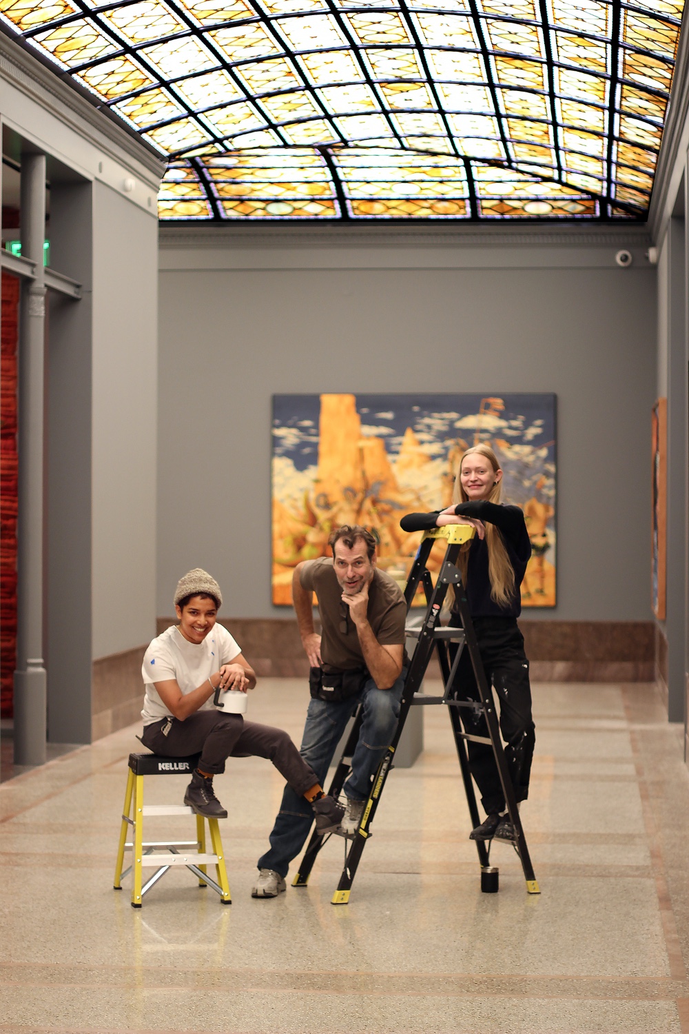 Three people stand on ladders in a grand marble hallway