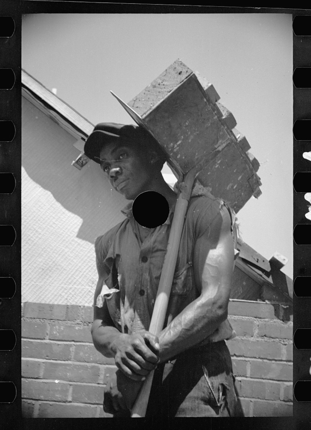 Bricklayer holding a skid of bricks over his shoulder in the sun
