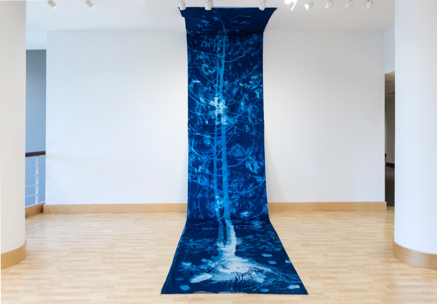 Blue image of a tree on dark fabric hanging from a wall onto the wooden floor