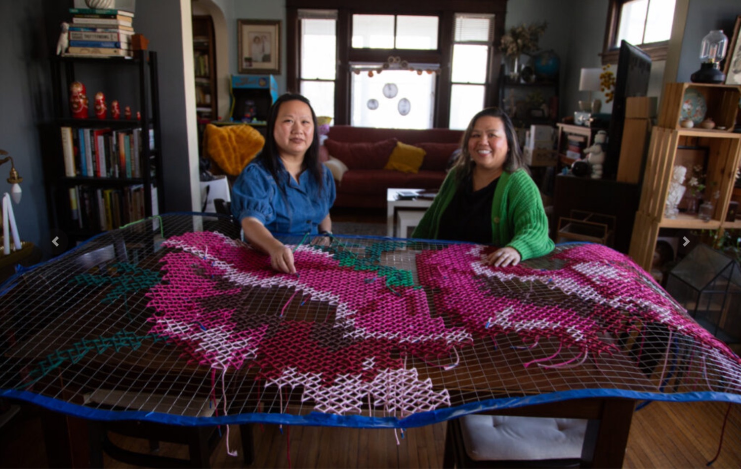 Two smiling women with a large cross-stitch of flowers