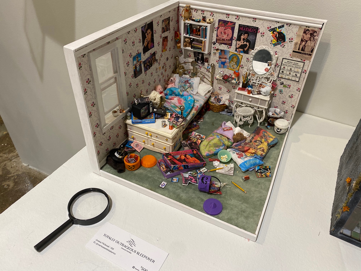 Miniature model bedroom on pedestal with magnifying lens.