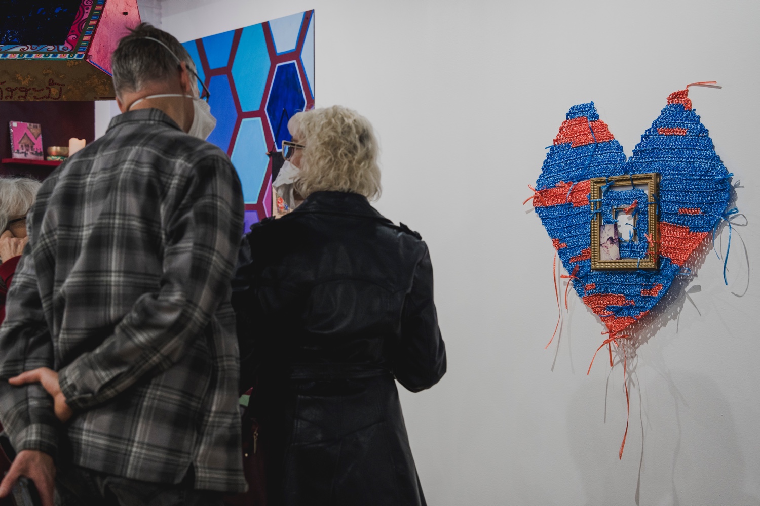 Visitors at an art gallery look at artwork shaped like a large blue and red heart