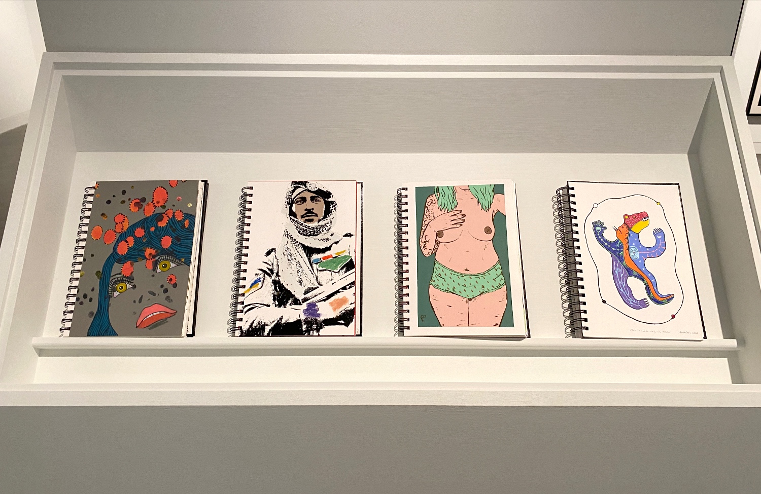 Four sketchbooks on display with different artworks on each page