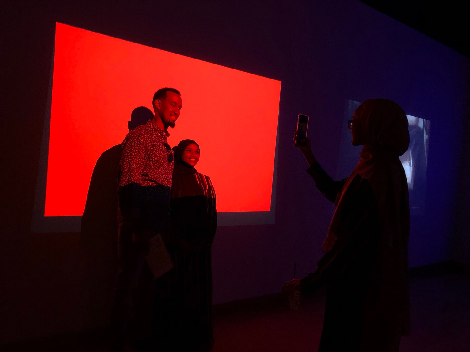 People posing for photo in front of red light projection