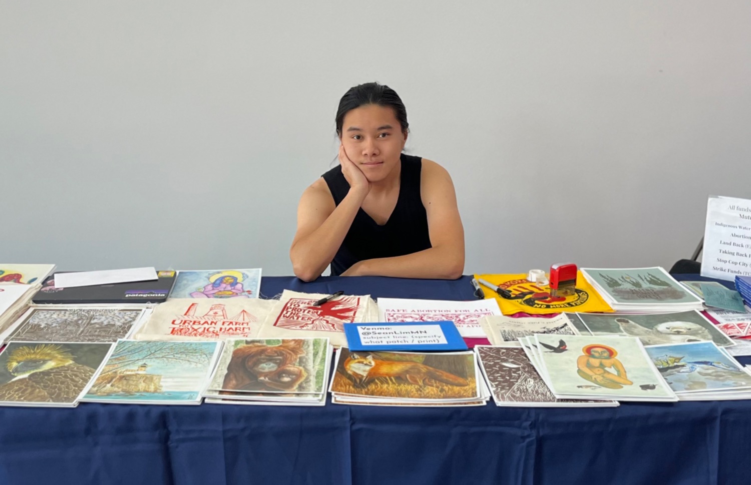 Person sits at a table full of artwork.