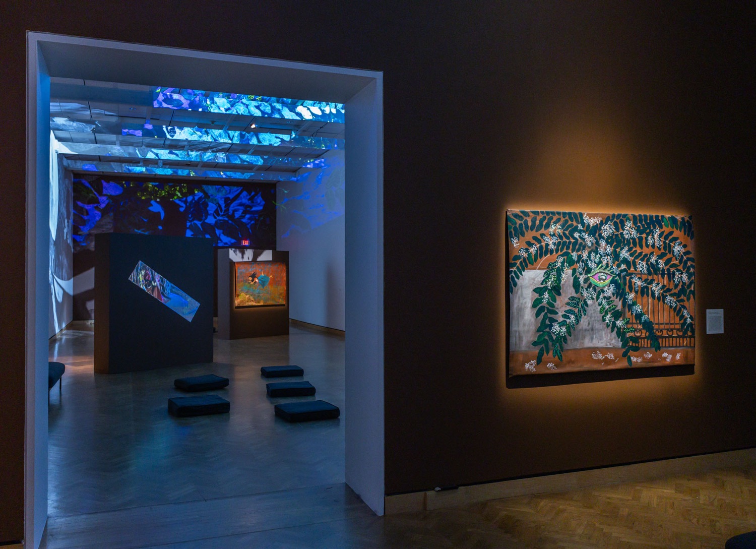 Painting of a plant with a pink and green eye next to a doorway into a museum gallery with colorful projections