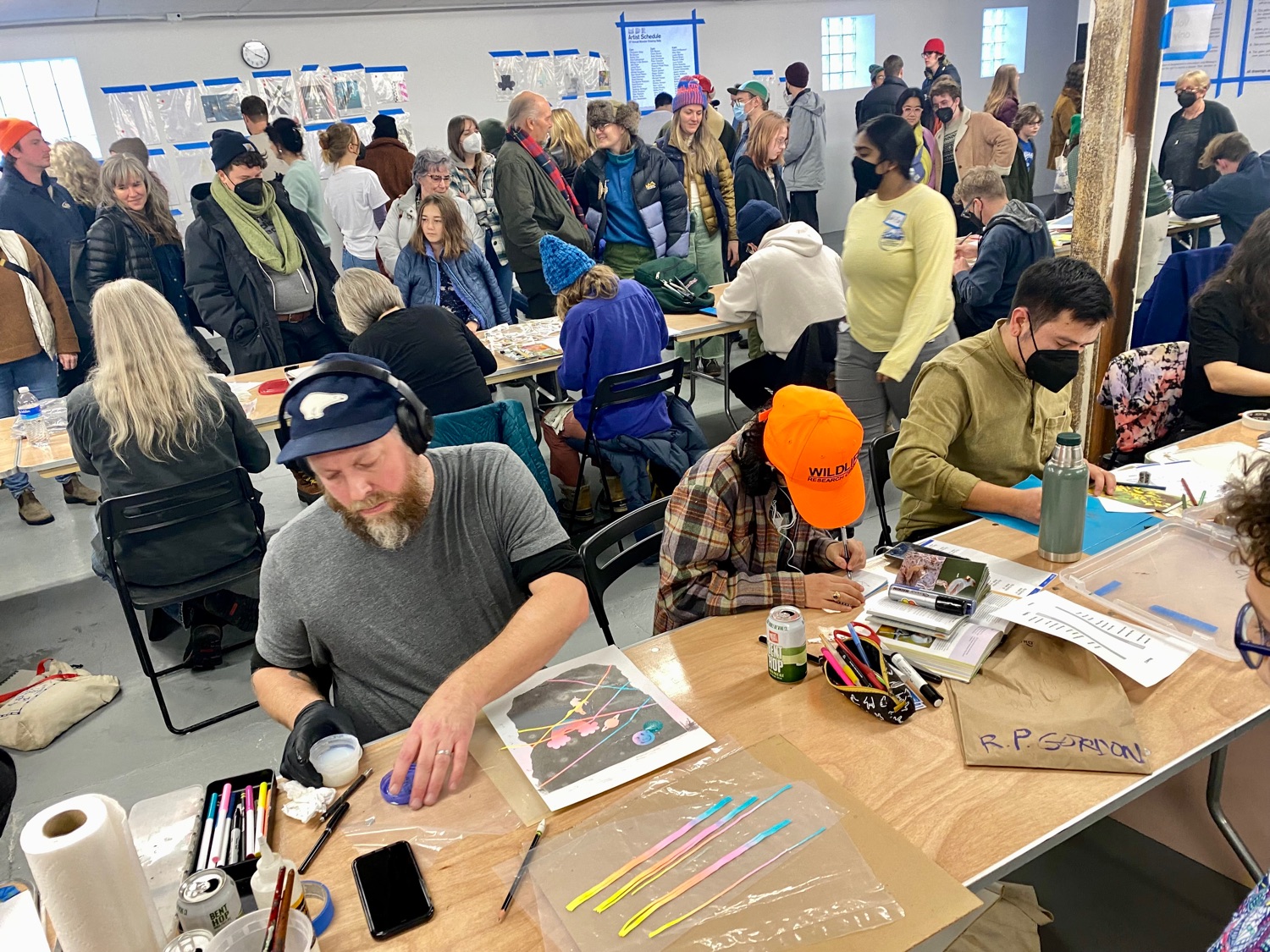 Artists work at tables while audience members walk by and observe
