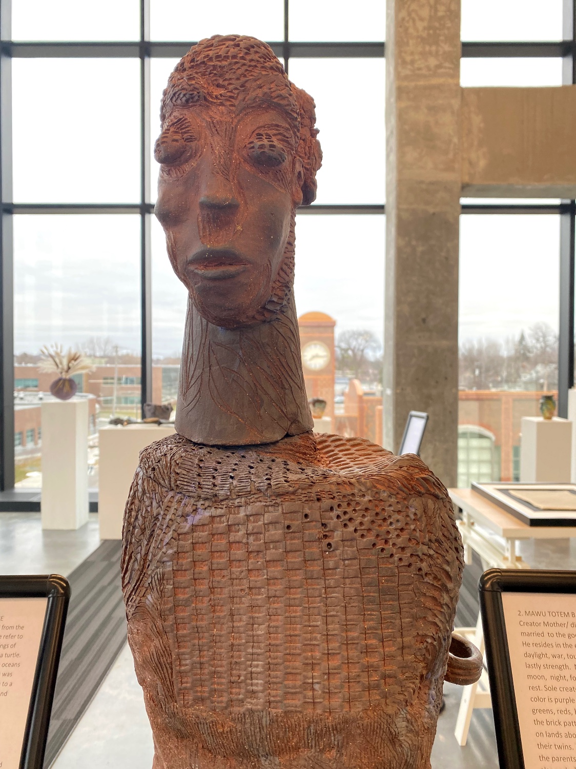 Ceramic sculpture of a head with a long neck on top of a woven basket-like shape