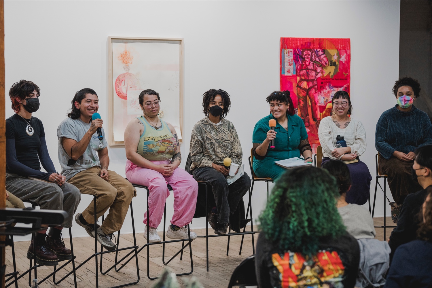 A panel of 7 people with microphones talk and smile in front of a crowd