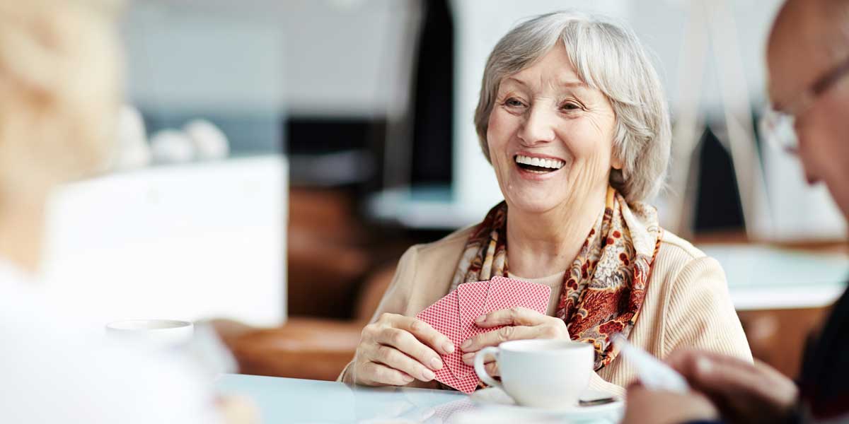 a senior woman laughs as she plays cards with friends