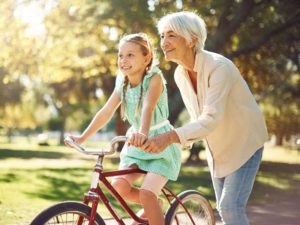 a senior woman helps her granddaughter ride a bike