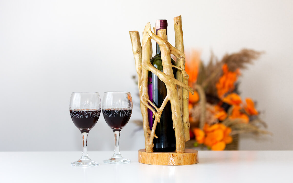 Artistic wine bottle holder made out of wood posed next to two wine glasses