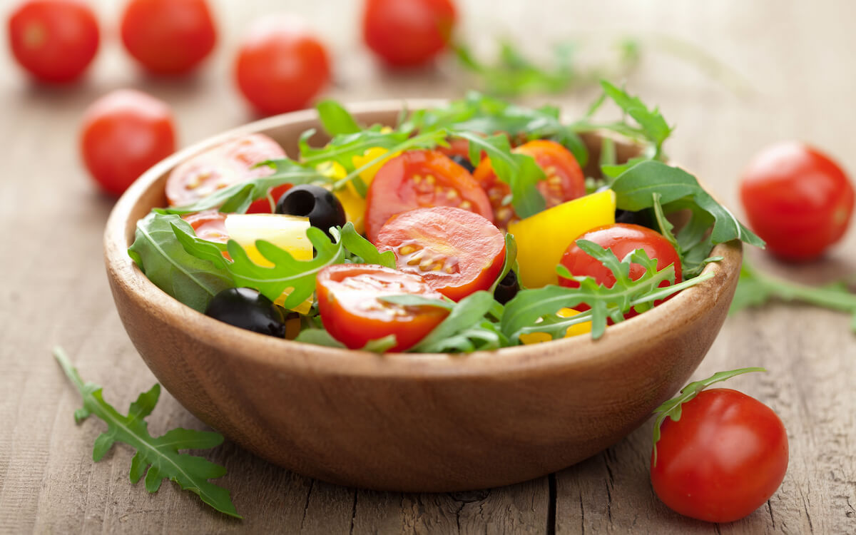 Wooden salad bowl filled with salad and surrounded by tomatoes