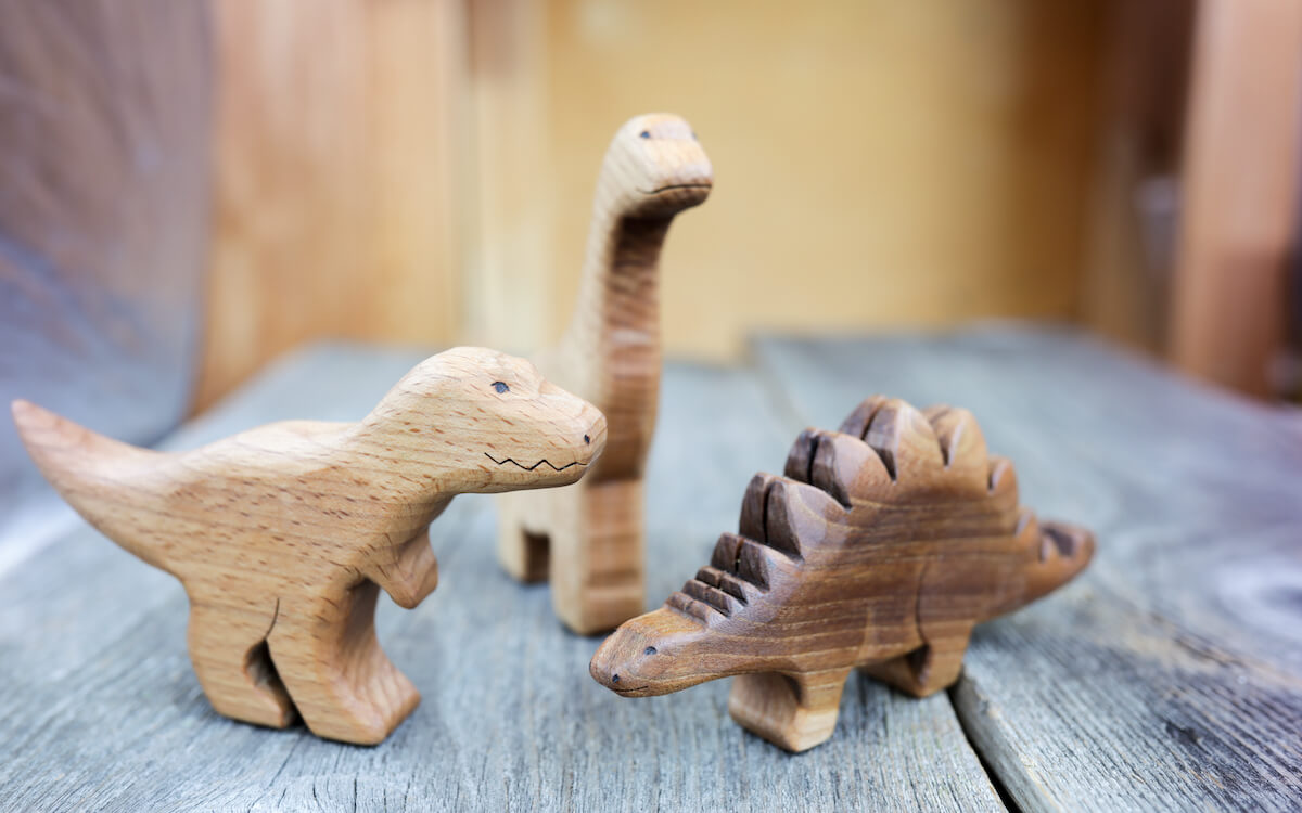 Wooden dinosaur toys in the shapes of a Tyrannosaurus rex, stegosaurus, and brachiosaurus