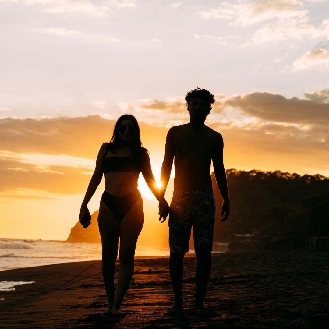 Silhouette of a couple holding hands at sunset on a beach in El Salvador, with golden sky and waves. Silhouette of a couple holding hands at sunset on a beach in El Salvador, with golden sky and waves.