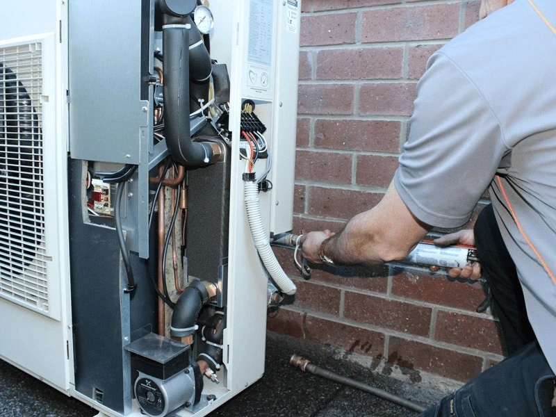 a technician repairing an HVAC unit against a brick wall.