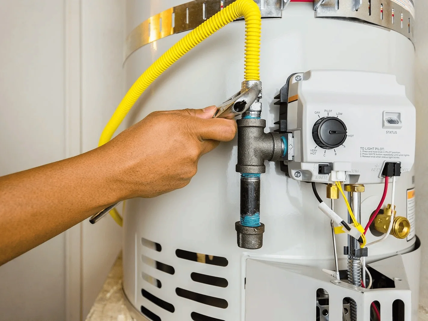 an HVAC expert using a wrench to repair a water heater with yellow gas line.
