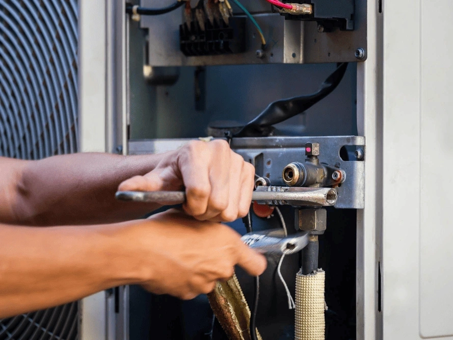 a technician using a wrench to repair an HVAC unit.