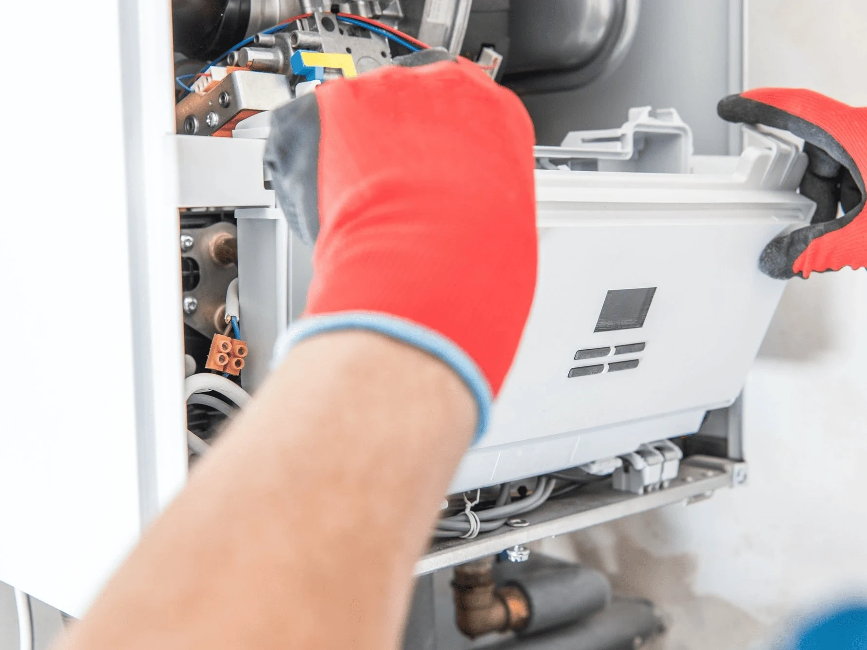 a technician wearing red gloves installing a component in an HVAC unit.