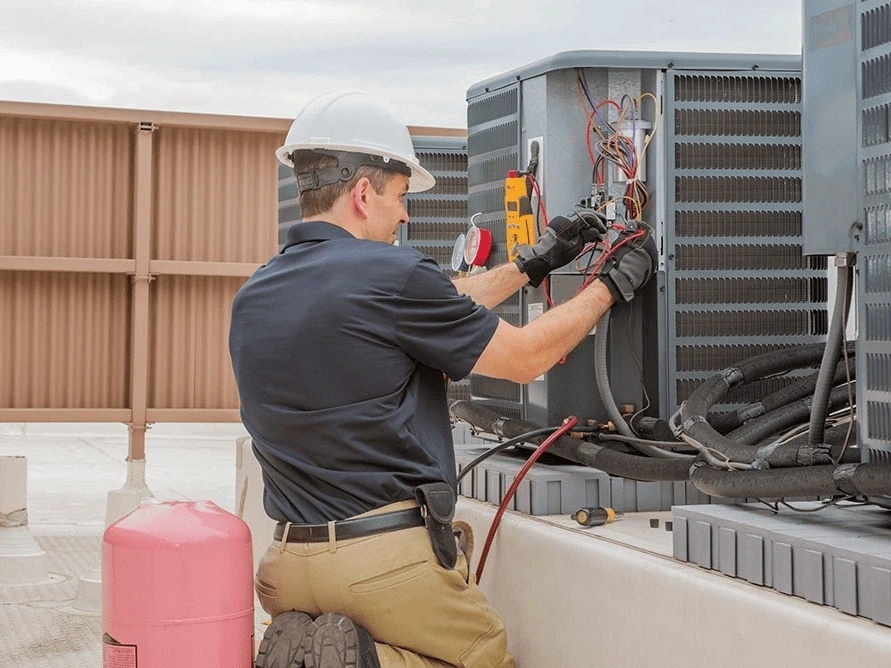 a technician in a hard hat repairing an HVAC unit on a rooftop.