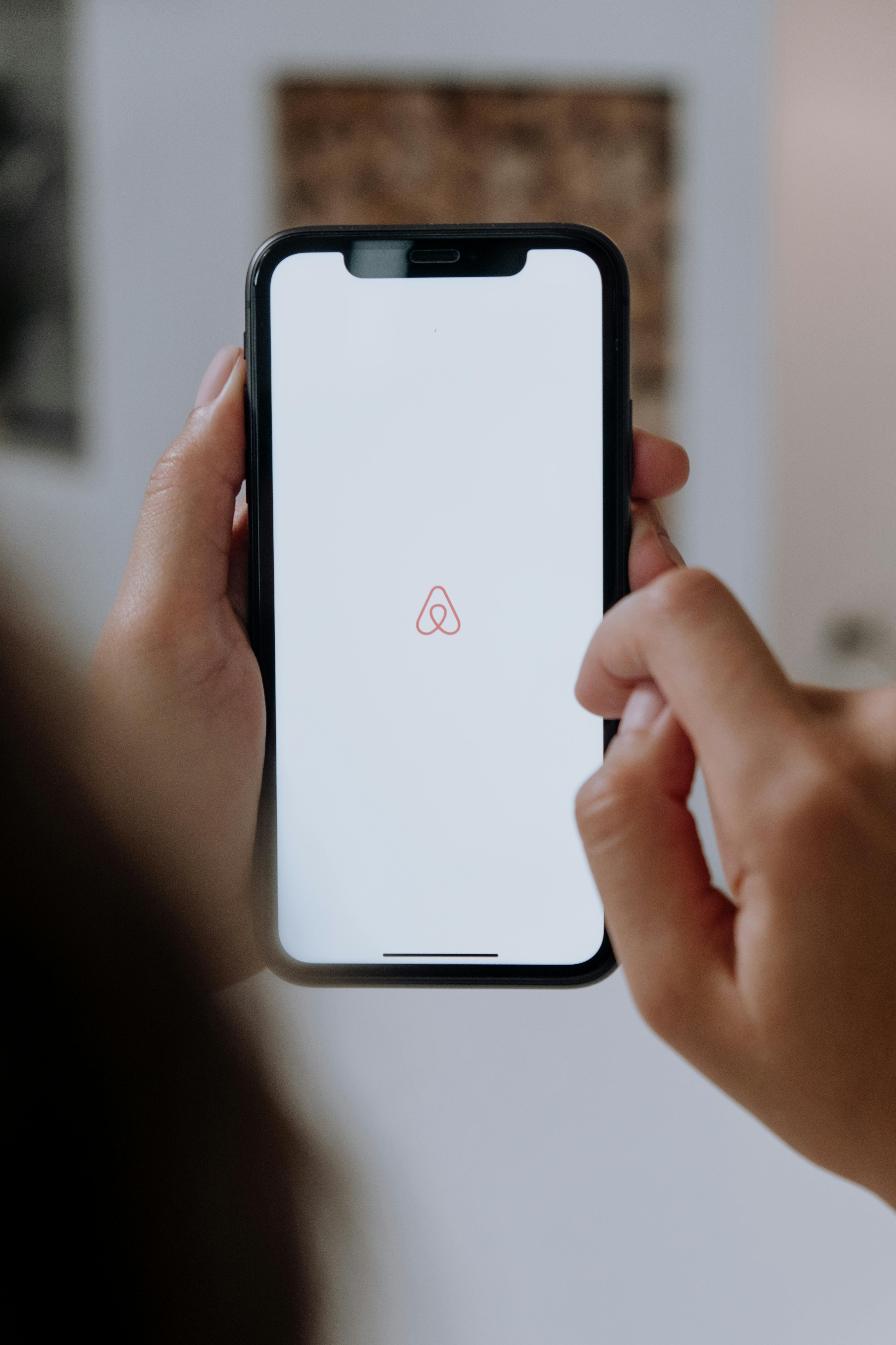 A person holding a smartphone displaying the Airbnb logo.