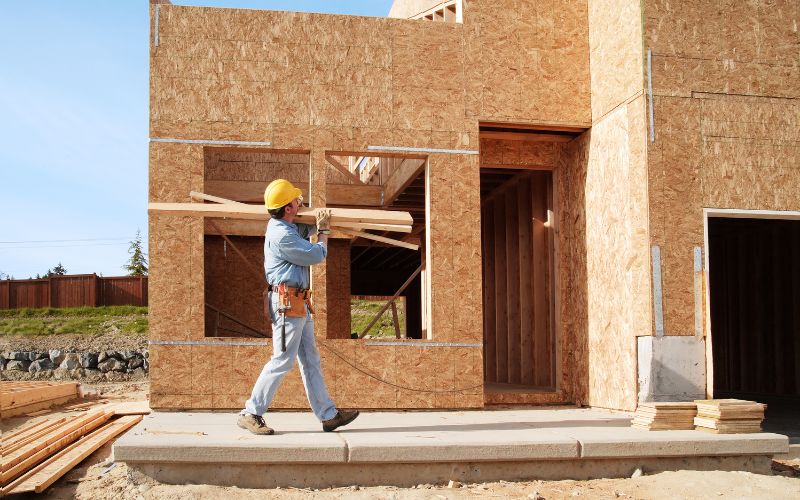 A man walking holding materials on an ADU construction site.