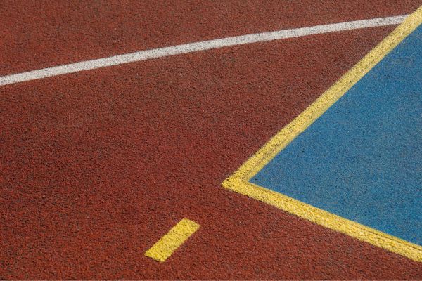 Close-up of outdoor sports court surface with red, blue, white, and yellow painted lines. Close-up of outdoor sports court surface with red, blue, white, and yellow painted lines.