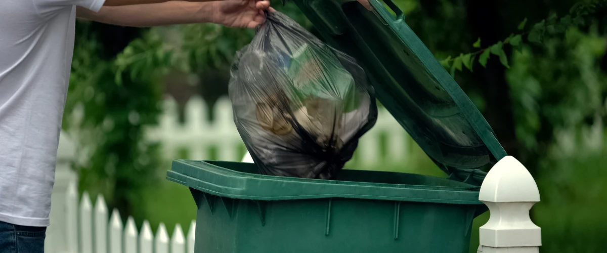 Person throwing garbage bag into residential trash bin Person throwing garbage bag into residential trash bin