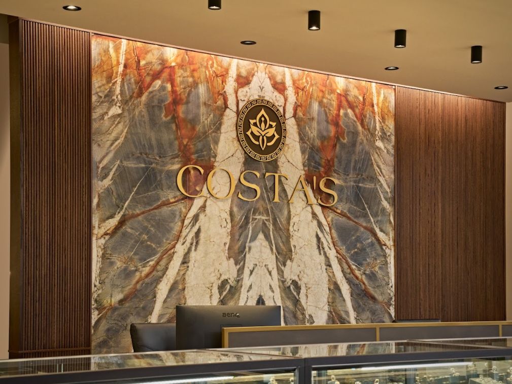 Image shows a luxurious, modern interior with a prominent marble wall featuring the logo "COSTA'S" in elegant gold lettering. The design includes stylish lighting and wooden accents, creating a sophisticated atmosphere. Image shows a luxurious, modern interior with a prominent marble wall featuring the logo "COSTA'S" in elegant gold lettering. The design includes stylish lighting and wooden accents, creating a sophisticated atmosphere.