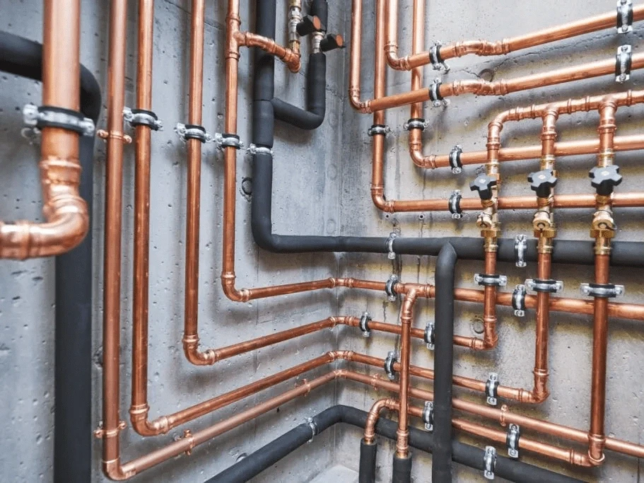 a copper and black plumbing pipes intricately arranged along a concrete wall, featuring valves and fittings.
