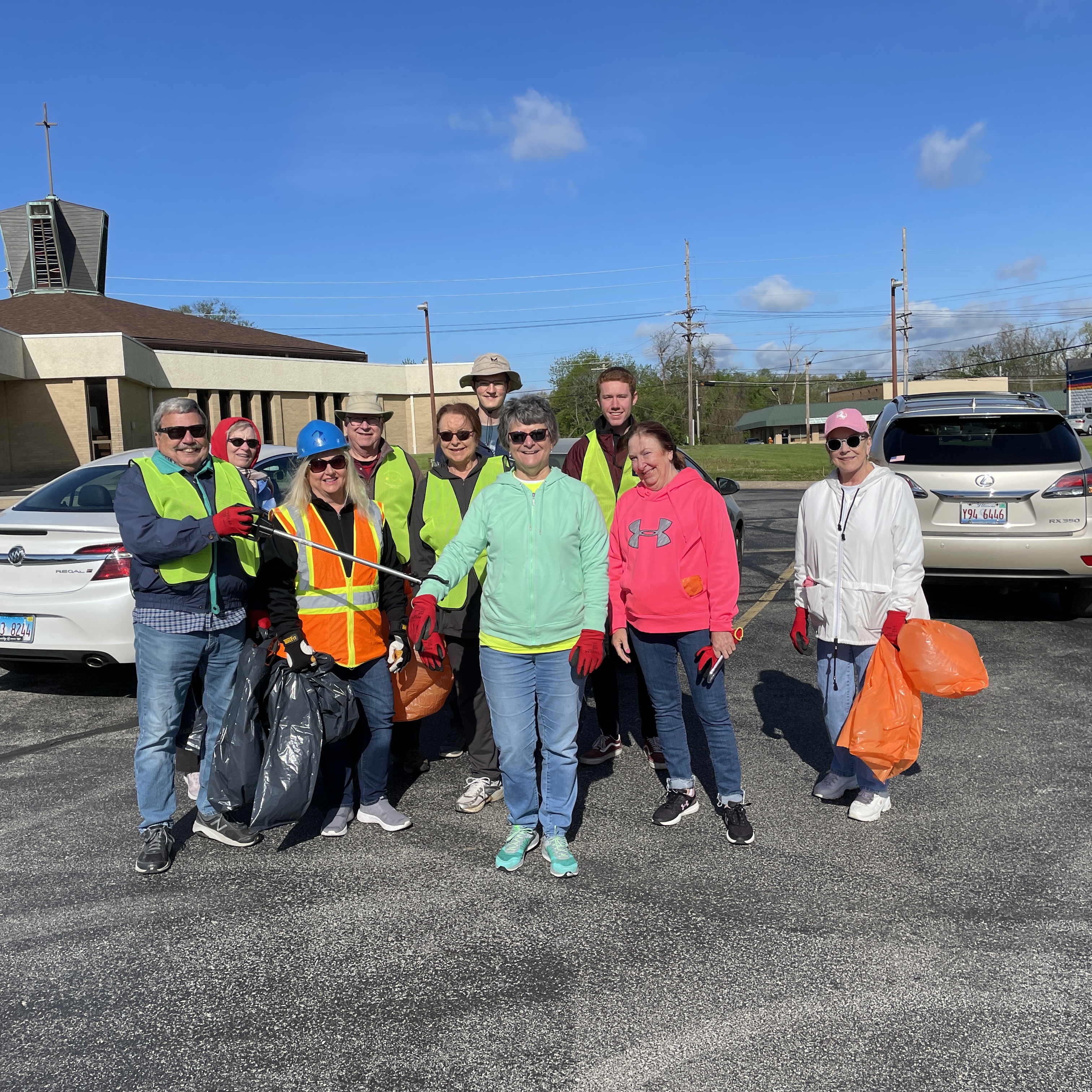Rotarians from Riverbend and Alton Rotary clubs stand together, smiling and holding large trash bags, ready to clean the streets of Alton during the Annual City-Wide Cleanup event.