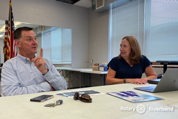 Gene Howell, seated and passionately discussing the mission and impact of Riverbend Head Start, with Rotary Club President Monica Bristow attentively listening to his presentation.