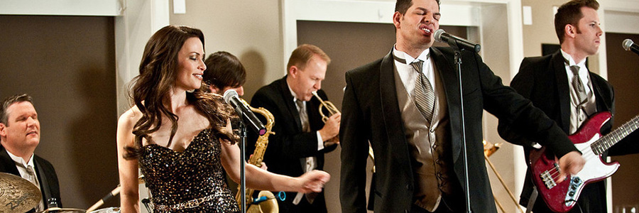 Wedding Band (two singers, bass player, drummer, saxophone player, trumpet player) Dressed in Formal Wedding Attire and Performing at Wedding Reception with PA system and Microphones.