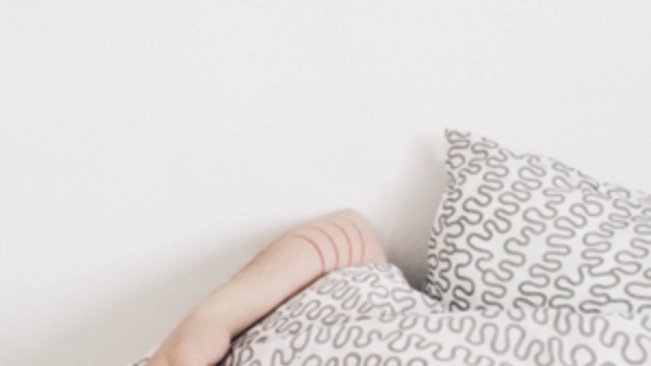 An arm poking out from under a beige and white duvet