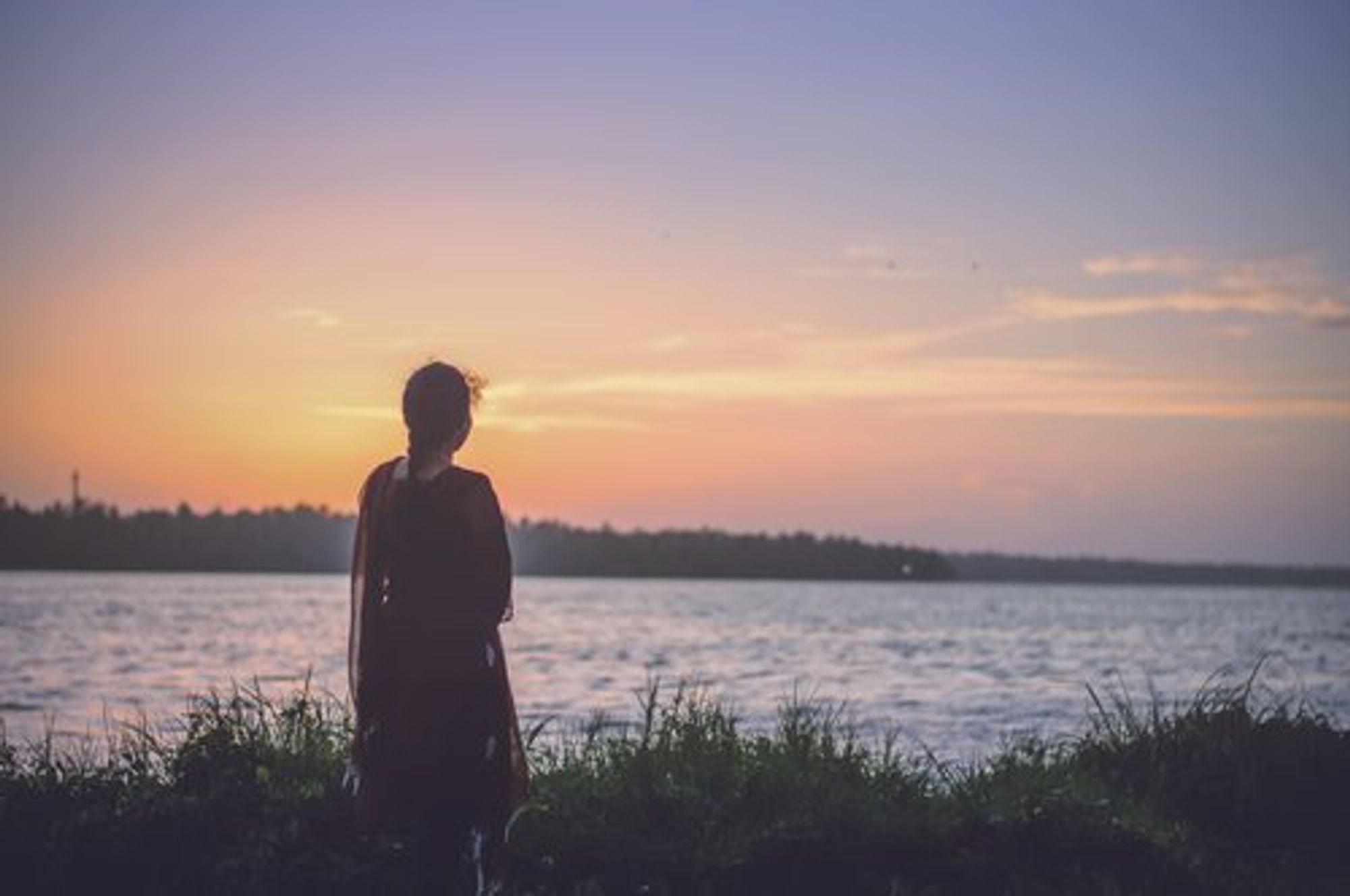 Silhouette of a woman overlooking a calm lake at sunset