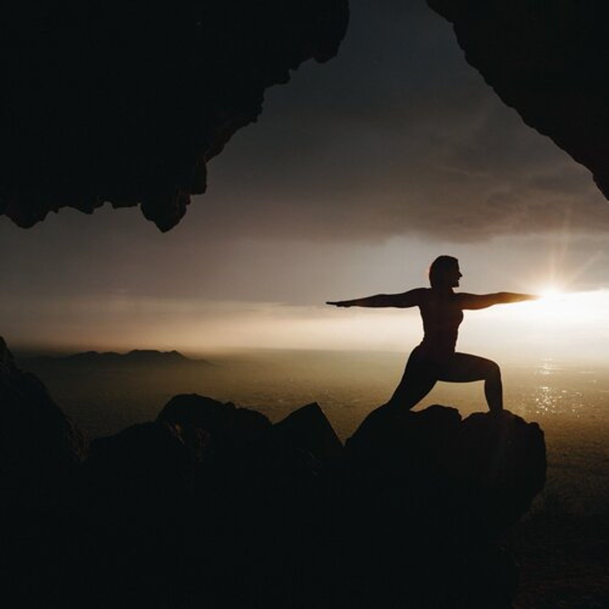 Silhouette of a person standing in warrior yoga pose in front of a sunset