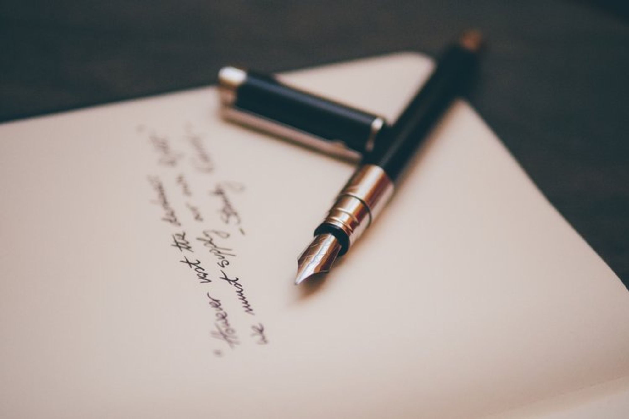 Cream coloured paper with a black and gold ink pen and it's lid resting next to some black handwritten script Cream coloured paper with a black and gold ink pen and it's lid resting next to some black handwritten script