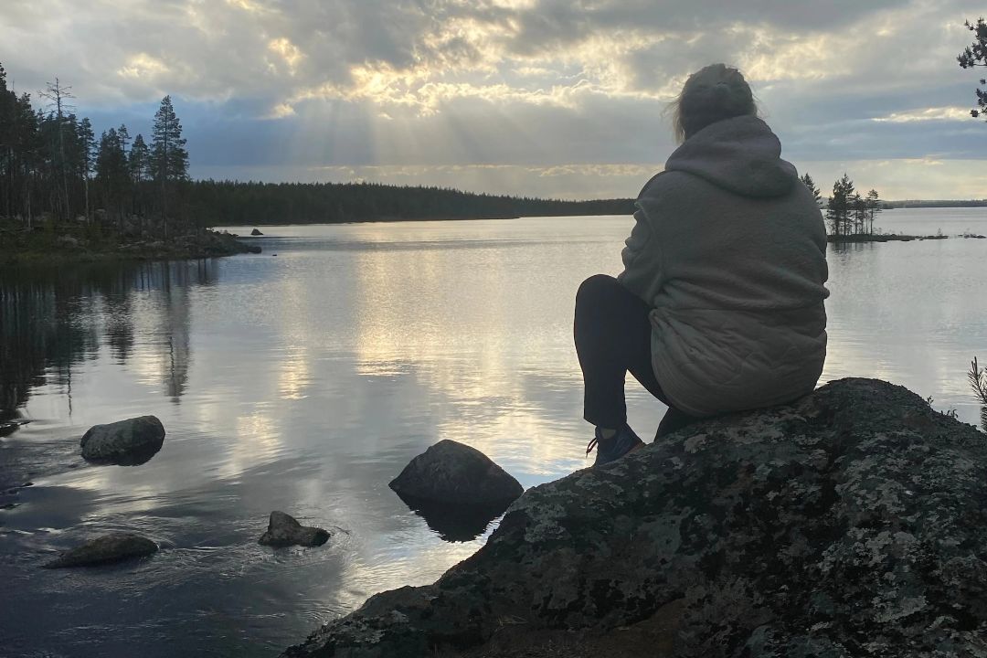 Johanna sitter på en klippa och blickar ut över sjön.  