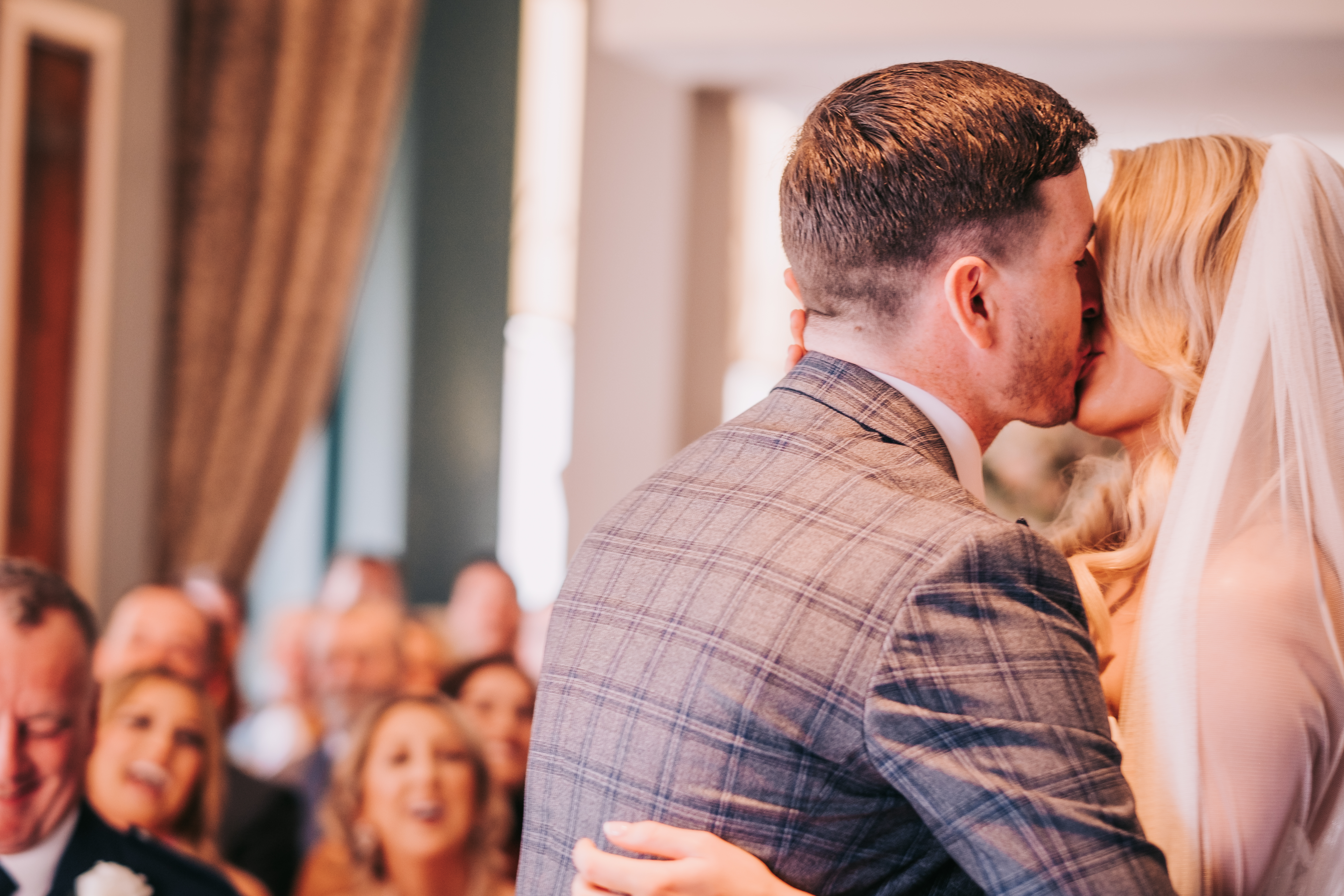 Bride and groom first kiss during ceremony, guests reacting in background Bride and groom first kiss during ceremony, guests reacting in background