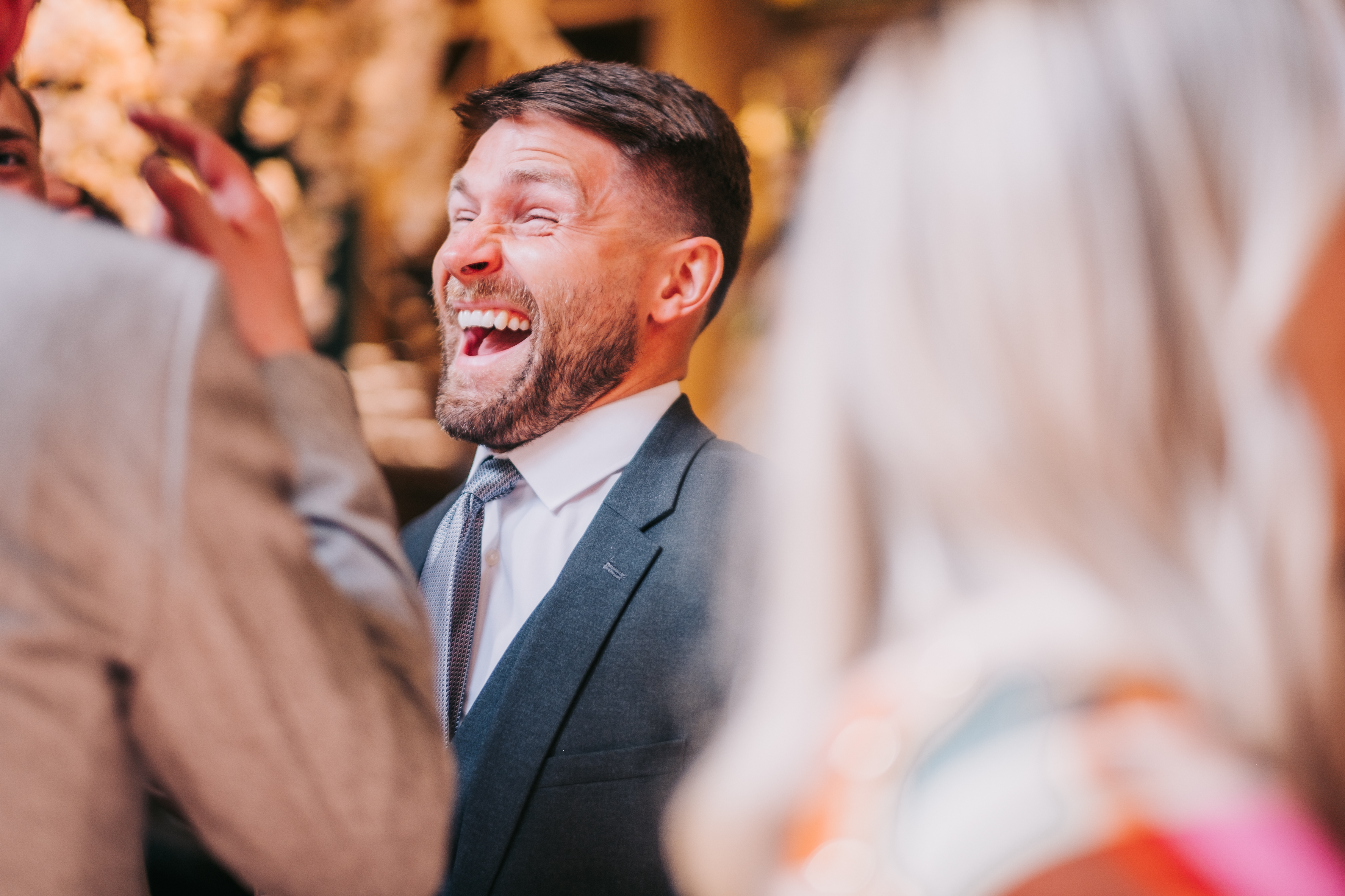 Wedding guest in grey suit mid-laughter, natural candid shot during drinks reception. Wedding guest in grey suit mid-laughter, natural candid shot during drinks reception.